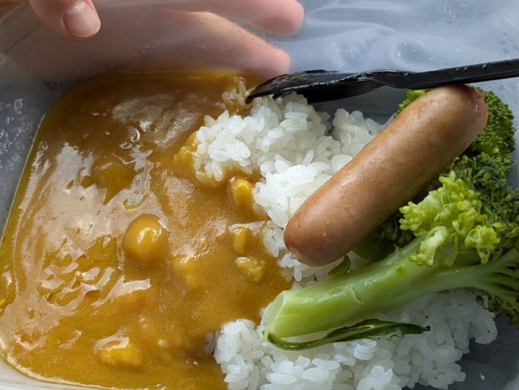 炊きあがった米にカレー、ソーセージ、ブロッコリーを乗せてる画像