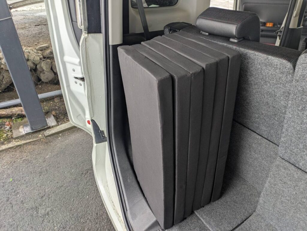 軽自動車の荷台に畳んだマットレス意を立てて置いている画像