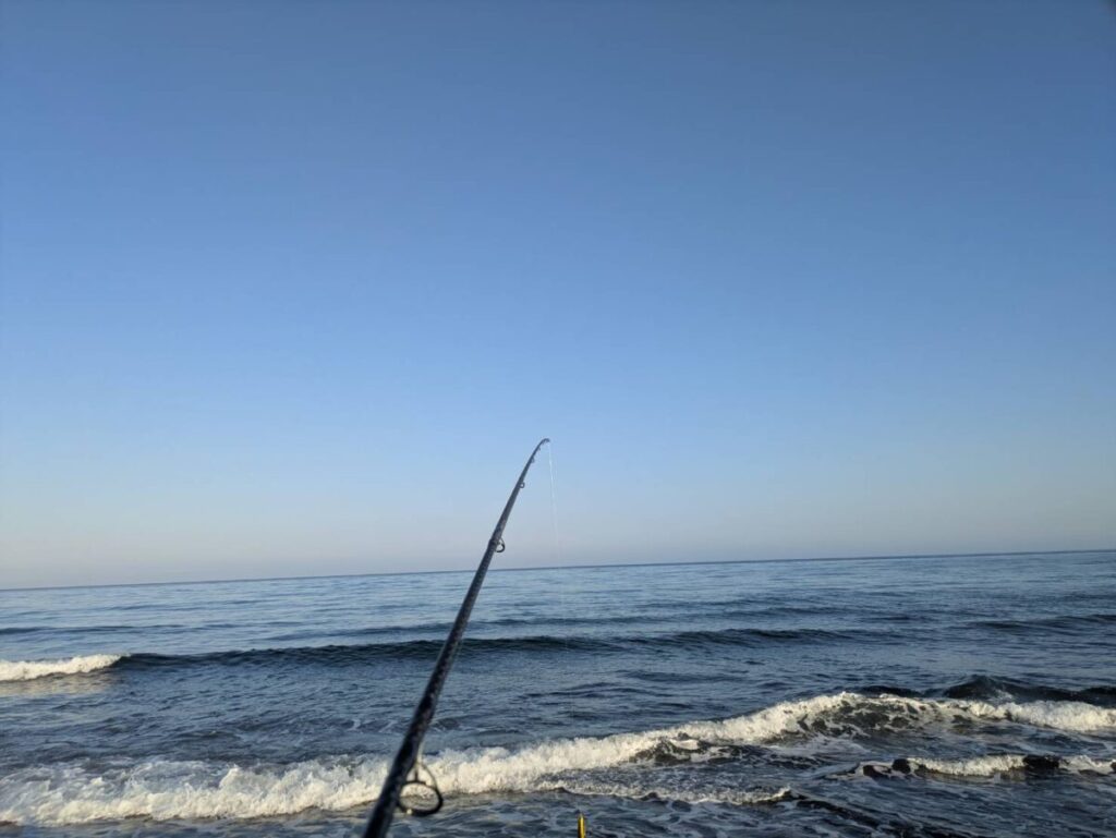 朝焼けの中、釣り竿を持って海に向かっている画像。