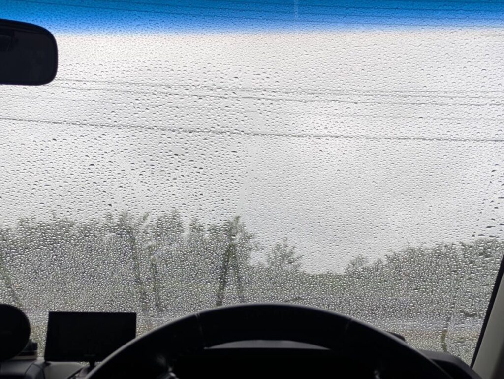 車の運転席から外を見ている様子。ガラスに雨が降って水滴が沢山ついている。